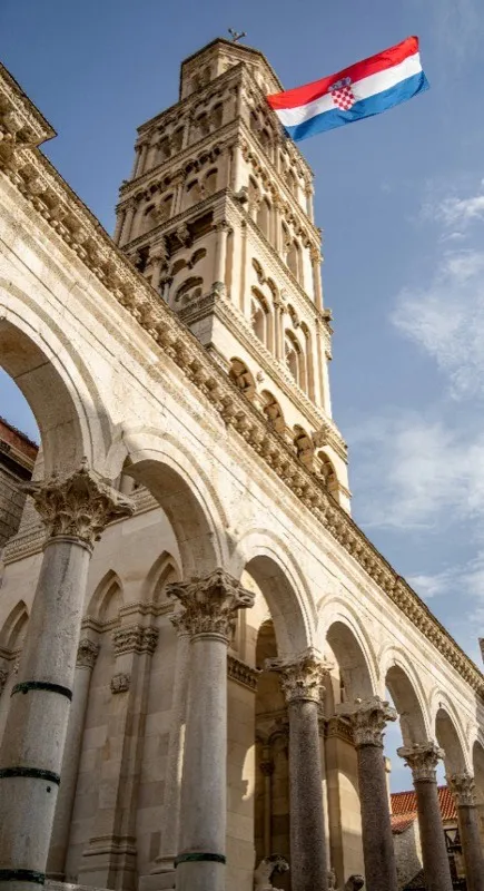 Zvonik katedrale u Splitu s hrvatskom zastavom, kroz antičke kamene lukove